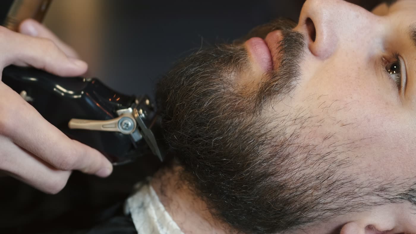 Cliente de barba cheia sentado em cadeira de barbearia