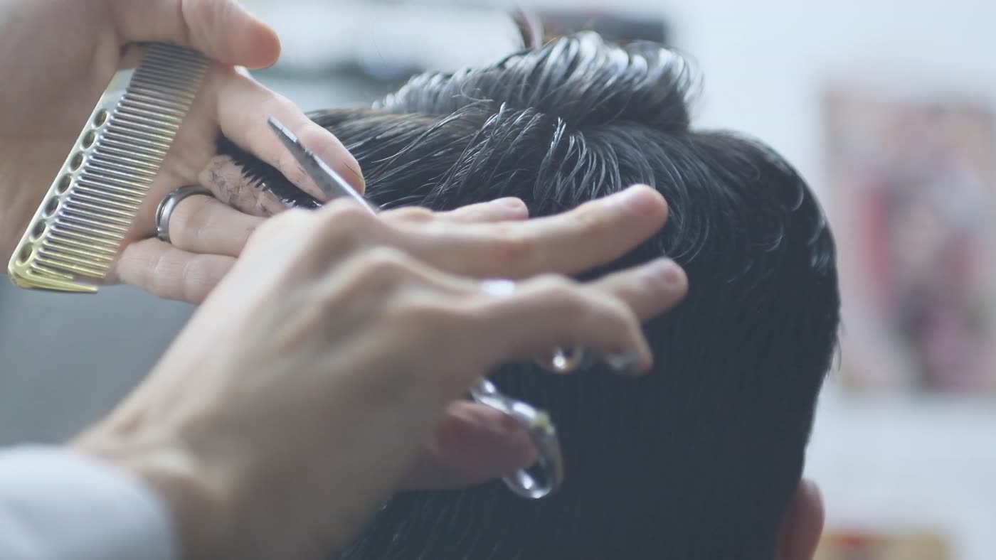 Mãos de profissional trabalhando com pente e tesoura em cabelo escuro